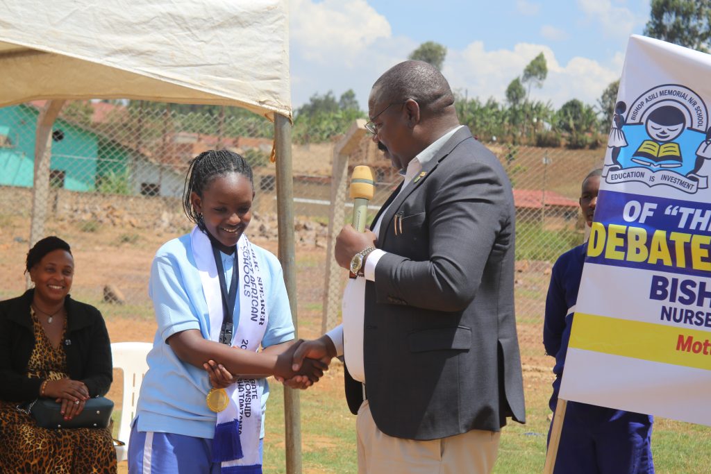 Kabale RDC Major Katamba Godfrey shakes hands with Dinah Igiraneza, a P7 pupil at Bishop Asil Nursery and PS and the best Junior East African debator.